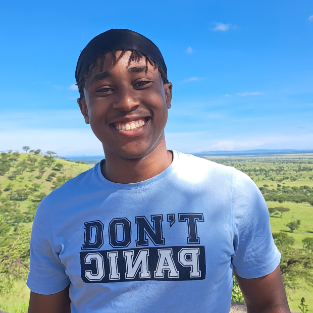 Dennis stands in front of green trees and a bright blue sky, smiling at the viewer