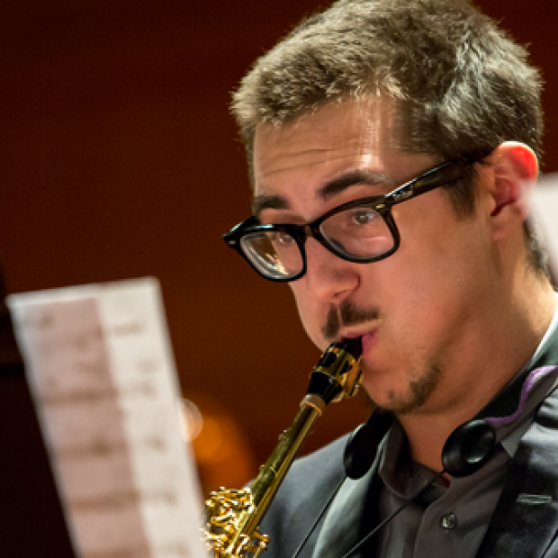 Man blowing into instrument with music scores on stands in the foreground