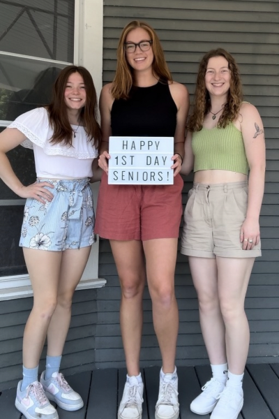 Three girls in shorts stand on the porch of a house